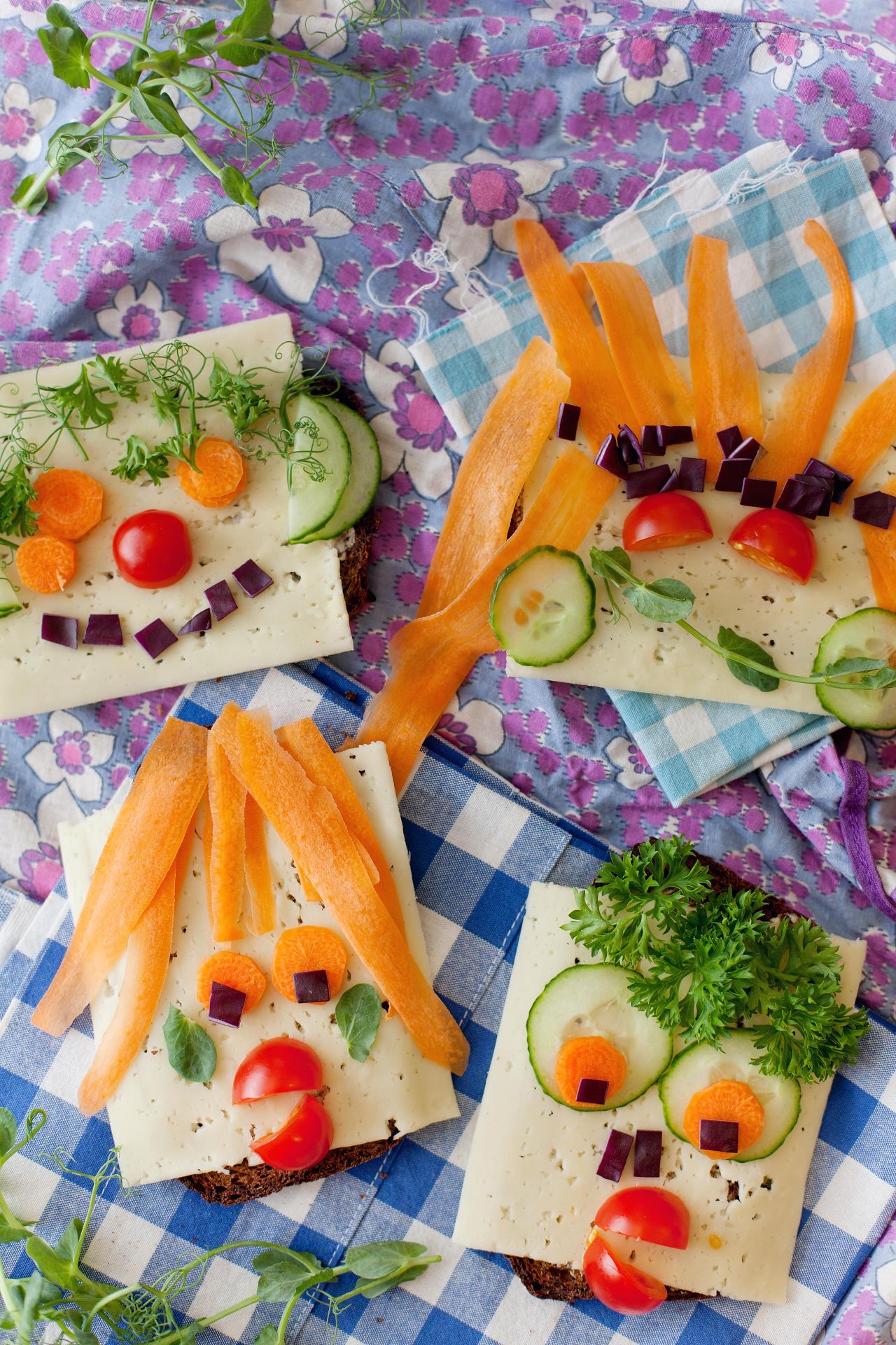 Bild på ostsmörgåsar där olika grönsaker sapar ett ansikte i smörgåsen.